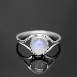 May include: A silver ring with a delicate design features a round moonstone gemstone.