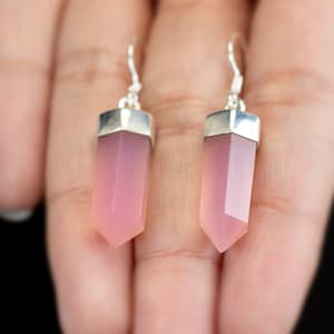 May include: A pair of silver dangle earrings with pink crystal teardrop shaped pendants.