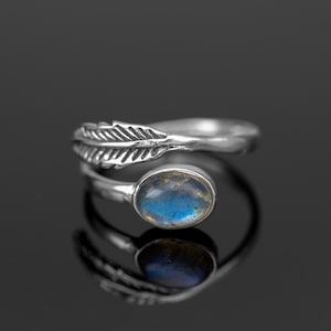 Può includere: Un anello d'argento con una pietra preziosa blu e un design a forma di piuma. L'anello è regolabile e può essere indossato su qualsiasi dito.