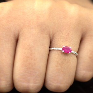 May include: A silver ring with a small oval-shaped pink gemstone set in the center. The ring has a beaded band.