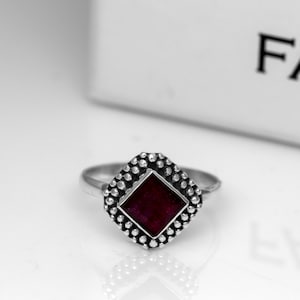 May include: A silver ring with a square-shaped red gemstone set in a textured silver bezel.