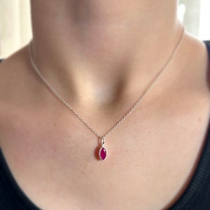 May include: A silver chain necklace with a small, red, marquise-shaped gemstone pendant.