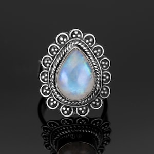 May include: A silver ring with a teardrop-shaped moonstone set in a decorative silver bezel. The ring has a detailed design with a beaded border.