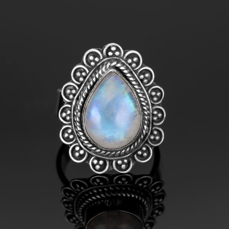 May include: A silver ring with a teardrop-shaped moonstone set in a decorative silver bezel. The ring has a detailed design with a beaded border.