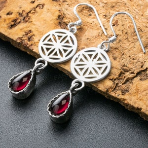 May include: A pair of silver earrings with a geometric design and a red gemstone drop. The earrings are made of sterling silver and feature a delicate, intricate pattern.