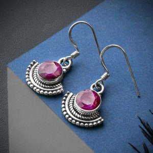 May include: A pair of silver earrings with a pink gemstone set in a decorative silver frame. The earrings have a hook closure.