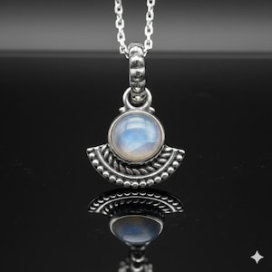 May include: A silver pendant necklace with a round, iridescent moonstone. The pendant has a fan-shaped design with leaf and bead details. The necklace chain is silver.