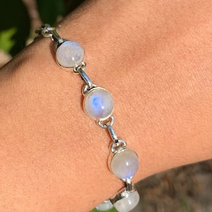 May include: A silver bracelet with round moonstone beads. The bracelet's links are silver, and the moonstones have a soft, milky appearance with subtle blue and white hues. The bracelet is designed to be worn on the wrist.