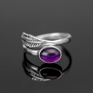 Puede incluir: Un anillo de plata con una piedra preciosa púrpura y un diseño de pluma.