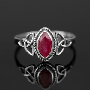 以下が含まれることがあります： ケルトの結び目のデザインに赤い宝石がセットされたシルバーリング