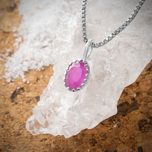 May include: A silver chain necklace with a pink gemstone pendant. The pendant is oval shaped and has a silver border.