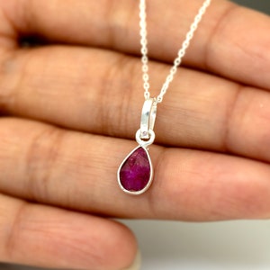 May include: A silver chain necklace with a teardrop-shaped pendant featuring a red ruby gemstone.