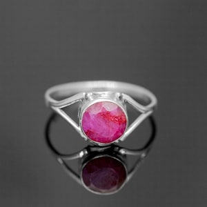 Peut inclure: Une bague en argent avec une pierre précieuse rose sertie dans un sertissage clos. La bague a un design simple et élégant.