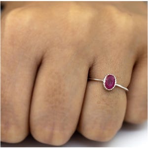 May include: A silver ring with a red oval gemstone. The ring is on a person's finger.