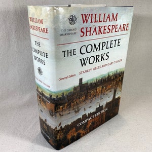 May include: A compact edition of "The Complete Works" by William Shakespeare. The book features a white cover with the title in red and black lettering. The cover also displays a detailed illustration of a cityscape. The book is a compact edition.