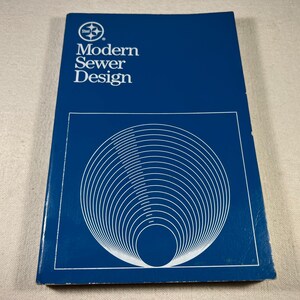 May include: A blue book with the title "Modern Sewer Design" on the cover. The cover also features a white circle with a compass design and a white abstract design of concentric circles.