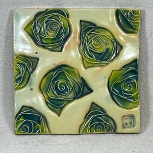 Puede incluir: Un azulejo de cerámica cuadrado con fondo blanco y un patrón repetitivo de rosas estilizadas verdes y azules.