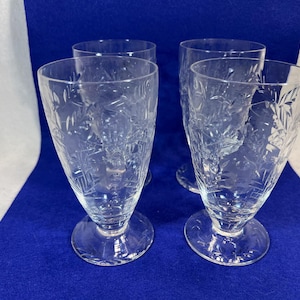 Puede incluir: Cuatro copas de vidrio transparente con un diseño de vidrio tallado. Las copas tienen una base redonda y un tallo alto y delgado.