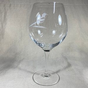 May include: A clear glass wine glass with an etched design of a bird on the side.