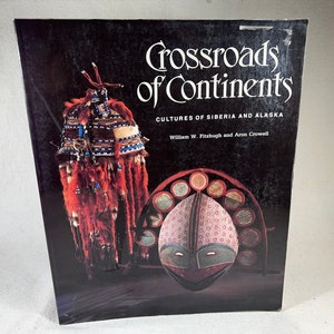 Może przedstawiać: Okładka książki "Crossroads of Continents: Cultures of Siberia and Alaska". Obraz przedstawia tradycyjne artefakty kulturowe syberyjskie i alaskańskie. Okładka jest przeważnie czarna z białym tekstem i zdjęciami maski i futrzanej odzieży.