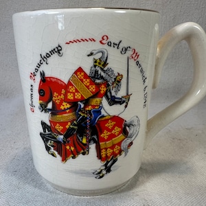 May include: White ceramic mug with a handle. The mug features a colorful illustration of a knight on horseback. The text on the mug reads "Thomas Beauchamp Earl of Warwick 1315-1346".