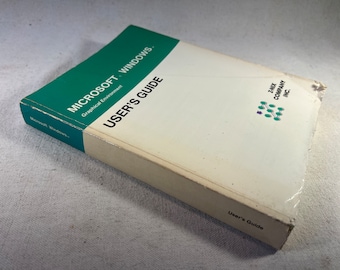 Pode incluir: Um livro branco com uma espinha verde intitulado "Microsoft Windows. Ambiente gráfico Guia do usuário". O livro está deitado sobre uma superfície branca.