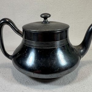 May include: A silver teapot with a rounded body and a lid with a knob. The teapot has a spout and a handle.