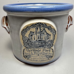 Könnte beinhalten: Eine weiße Keramikdose mit blauen und braunen Akzenten. Die Dose hat zwei Henkel und trägt ein Etikett mit dem Text "Heritage Park Bed & Breakfast Inn" und einer Zeichnung eines viktorianischen Hauses. Das Etikett enthält auch den Text "Victorian Lodging in Historic Old Town San Diego, California."