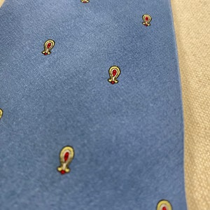 May include: A blue silk tie with a repeating pattern of small yellow and red paisley designs.