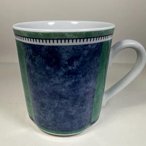May include: White ceramic mug with a curved handle. The mug features a blue and green design with a white interior. The mug has a green band at the top and bottom, and a blue marbled pattern in the centre.