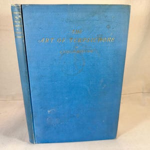 Puede incluir: Un libro antiguo titulado "The Art of Tortoiseshell" con una cubierta azul claro. El título y el nombre del autor están en letras doradas. El libro está ligeramente desgastado, lo que sugiere su edad e historia.