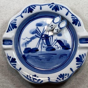 Könnte beinhalten: Ein blauer und weißer Aschenbecher aus Keramik mit einer holländischen Windmühlenszene und zwei kleinen Holzschuhen obenauf.