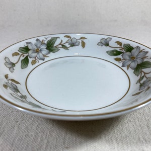 May include: A white ceramic bowl with a gold rim and a floral design featuring white flowers and green leaves.