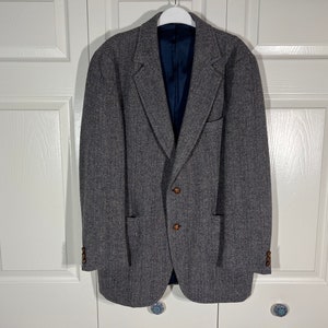May include: A gray herringbone blazer with two brown buttons. The blazer has a single chest pocket and two front pockets.