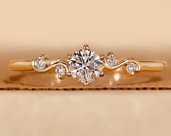 Könnte beinhalten: Ein goldfarbener Ring mit einem großen, runden, klaren Edelstein in der Mitte. Das Band hat ein zartes, wirbelndes Design mit kleineren, klaren Edelsteinen. Der Ring ist vor einem warmen, neutralen Hintergrund platziert.