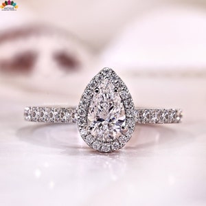 May include: A pear-shaped diamond engagement ring with a halo of smaller diamonds. The band is encrusted with small diamonds. The ring is set in a white metal, likely platinum or white gold.