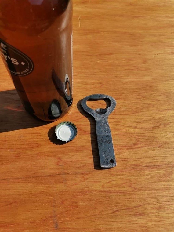 Blacksmith-forged steel bottle opener with a raw gunmetal finish — you can practically feel the hammer strikes in it.