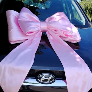 May include: A black car with a large pink satin bow on the bonnet. The car has a Hyundai logo on the front.