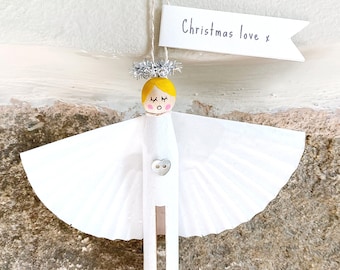 May include: A handmade angel ornament with a yellow head, white wings, and wooden body. The angel has a silver halo and a tag that reads "Christmas love x". The ornament is suspended by a string.
