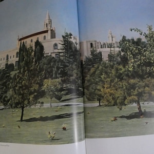 Puede incluir: Un edificio blanco con una alta aguja, rodeado de árboles verdes y un césped. El edificio tiene un techo rojo y muchas ventanas. Los árboles son altos y frondosos, y el césped está bien cuidado.