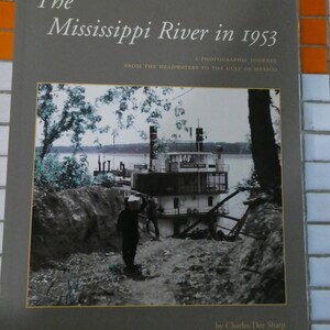 May include: A gray book cover with the title "The Mississippi River in 1953: A Photographic Journey from the Headwaters to the Gulf of Mexico" and the author "Charles Dee Sharp". The cover features a black and white photograph of a riverboat on the Mississippi River.