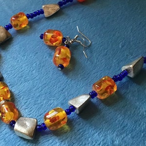 Moon pendant necklace set with orange and blue beads. Moon pendant with Celtic-like design and silver colored beads.