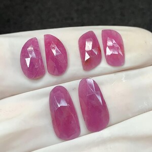 Pode incluir: Seis pedras preciosas rosas facetadas, em forma oval. As gemas estão dispostas em duas filas de três, com uma superfície polida e refletora. As pedras preciosas são de um tom rosa vibrante, com facetas internas visíveis.