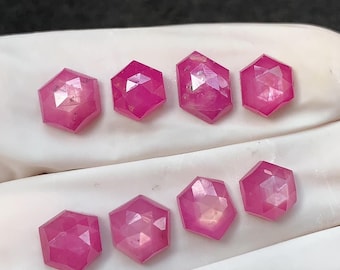 May include: Eight faceted, hexagonal-shaped, pink gemstones. The gems are a vibrant magenta color and appear to be cut with multiple facets, reflecting light. The gemstones are displayed on a white surface.