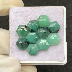 Puede incluir: Una colección de piedras preciosas de esmeralda facetadas en forma hexagonal, dispuestas en un patrón de panal. Las gemas varían en tonos de verde, desde el verde bosque profundo hasta tonos más claros, y se exhiben en una bandeja blanca.