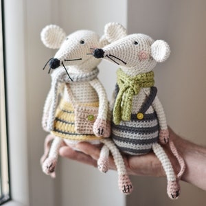 May include: Two crocheted mouse toys, one wearing a yellow and grey striped skirt and a pink bag, the other wearing a grey and white striped overall and a green scarf.