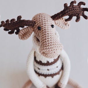 May include: A crocheted moose toy with brown antlers, a white and brown sweater, and black eyes.