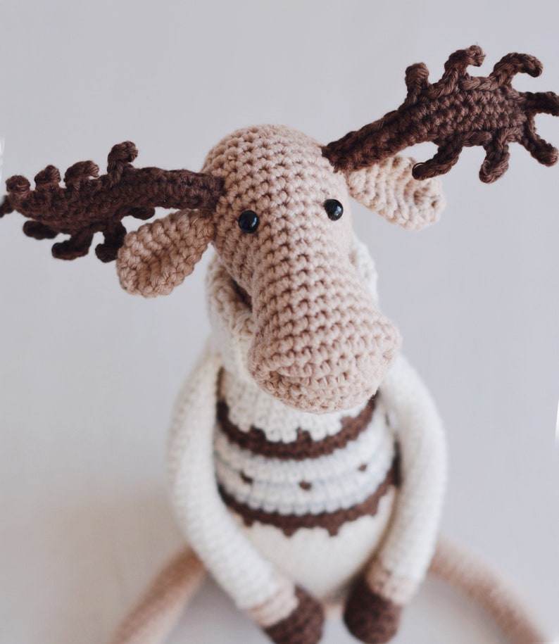 May include: A crocheted moose toy with brown antlers, a white and brown sweater, and black eyes.