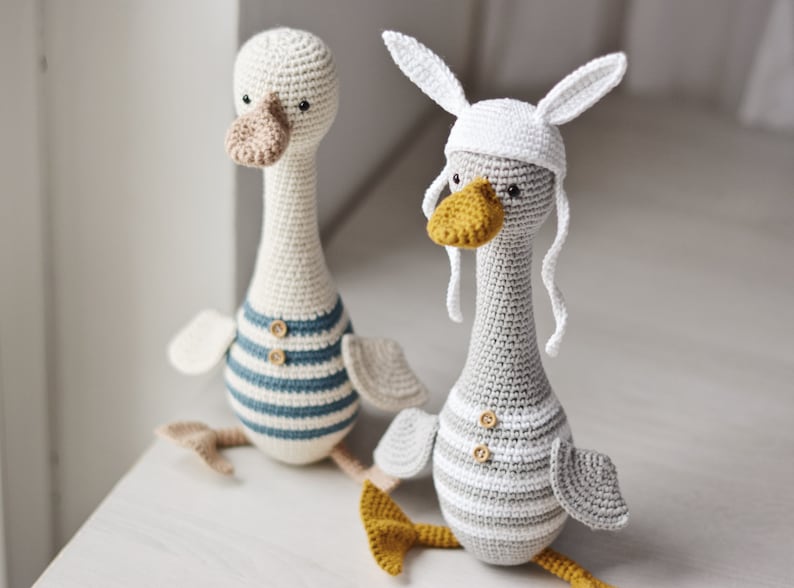 Peut inclure: Deux peluches de canards en crochet, l'une blanche avec une chemise ray&eacute;e bleu et blanc et l'autre grise avec une chemise ray&eacute;e blanc et gris. Les deux ont un bec jaune et des yeux noirs.