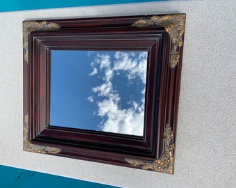 May include: A dark wood framed mirror with ornate gold accents. The mirror reflects a blue sky with white clouds.